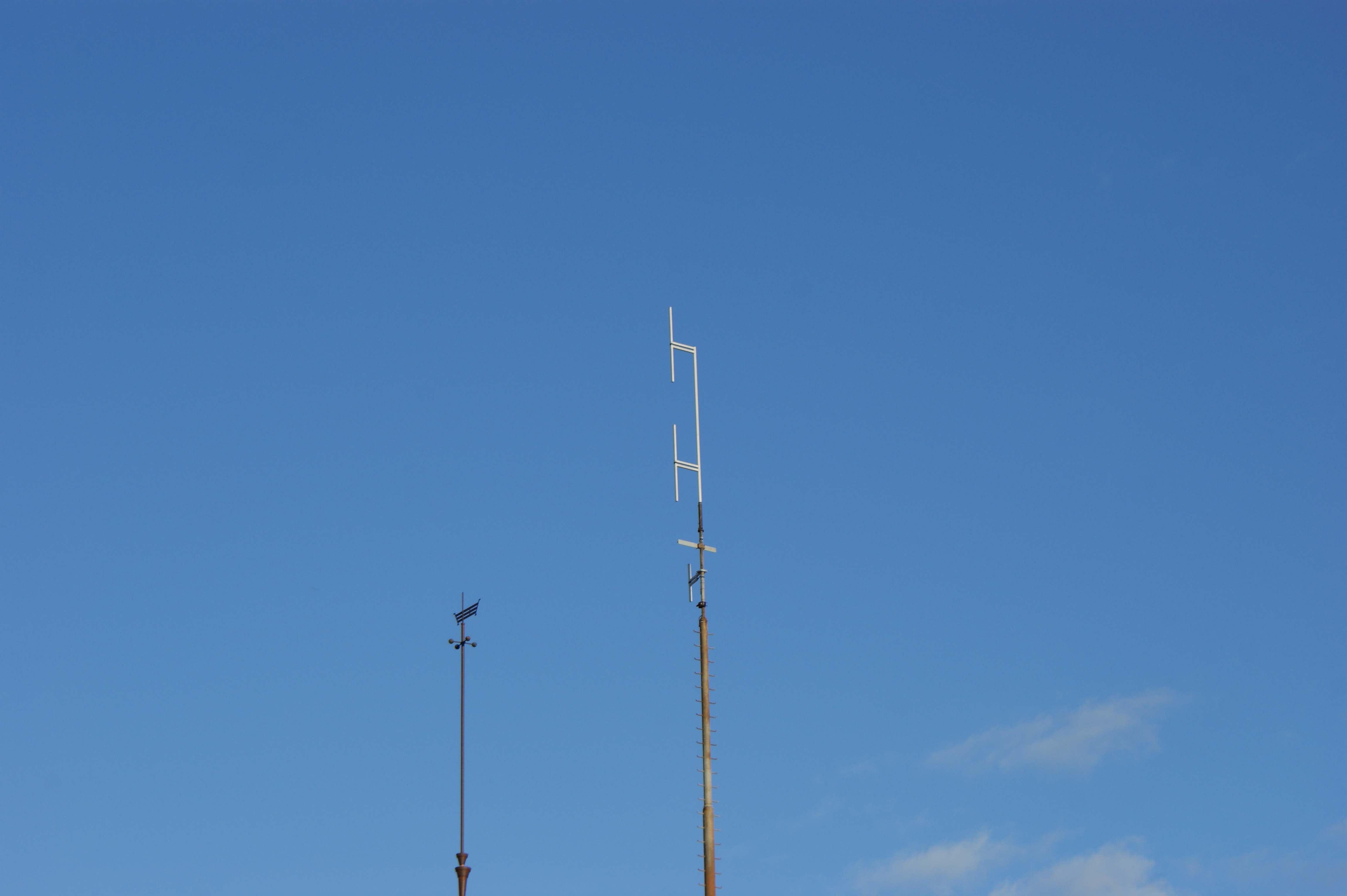 Figure 6 — Two vertical dipole antenna elements mounted on a mast (the gray H-braced elements partway up the pole), shown against a lightning-rod-tipped mast for scale. Photo: File:Vertical dipole antenna.jpg…