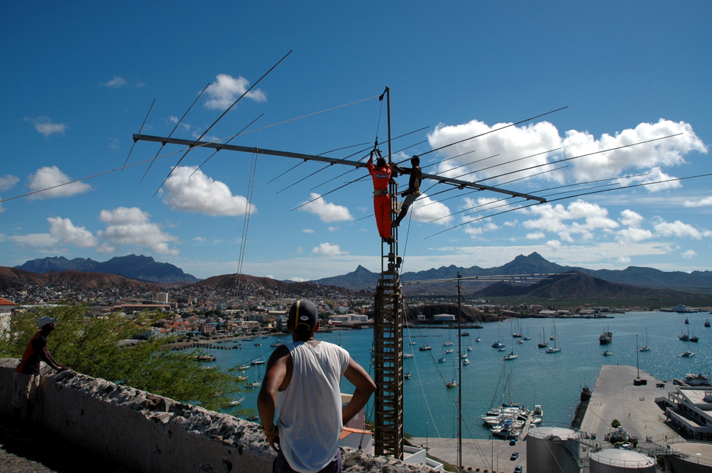 Figure 1 — Installing a large HF Yagi on a rooftop tower overlooking a harbor — the deployment half of this volume's job, not just the cutting list. Photo: File:Antenna d44ac.jpg, author not machine-readable …